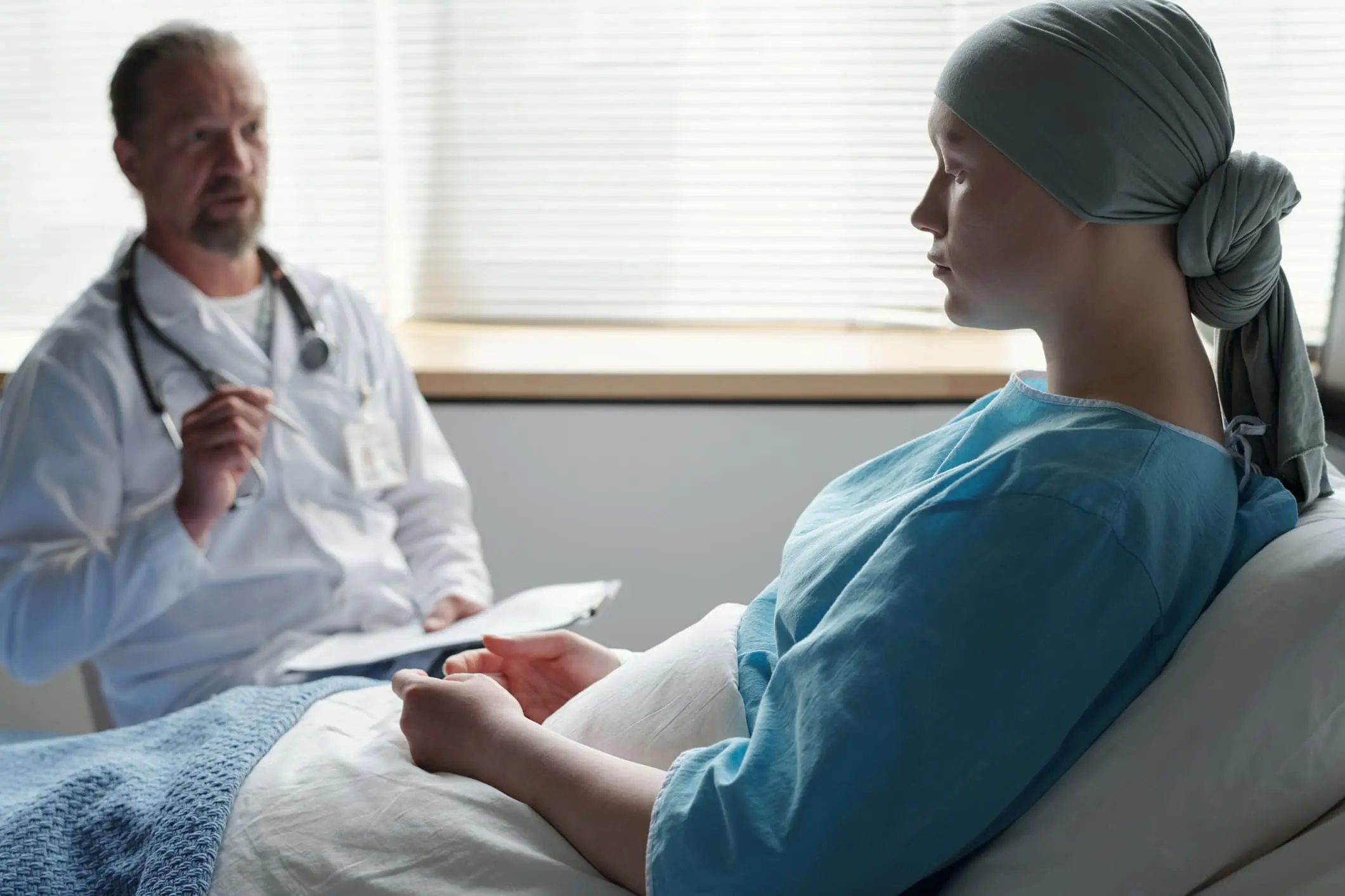 Paciente oncológica con pañuelo en la cabeza recibiendo orientación emocional de un médico en consulta hospitalaria, antes o después de una cirugía.