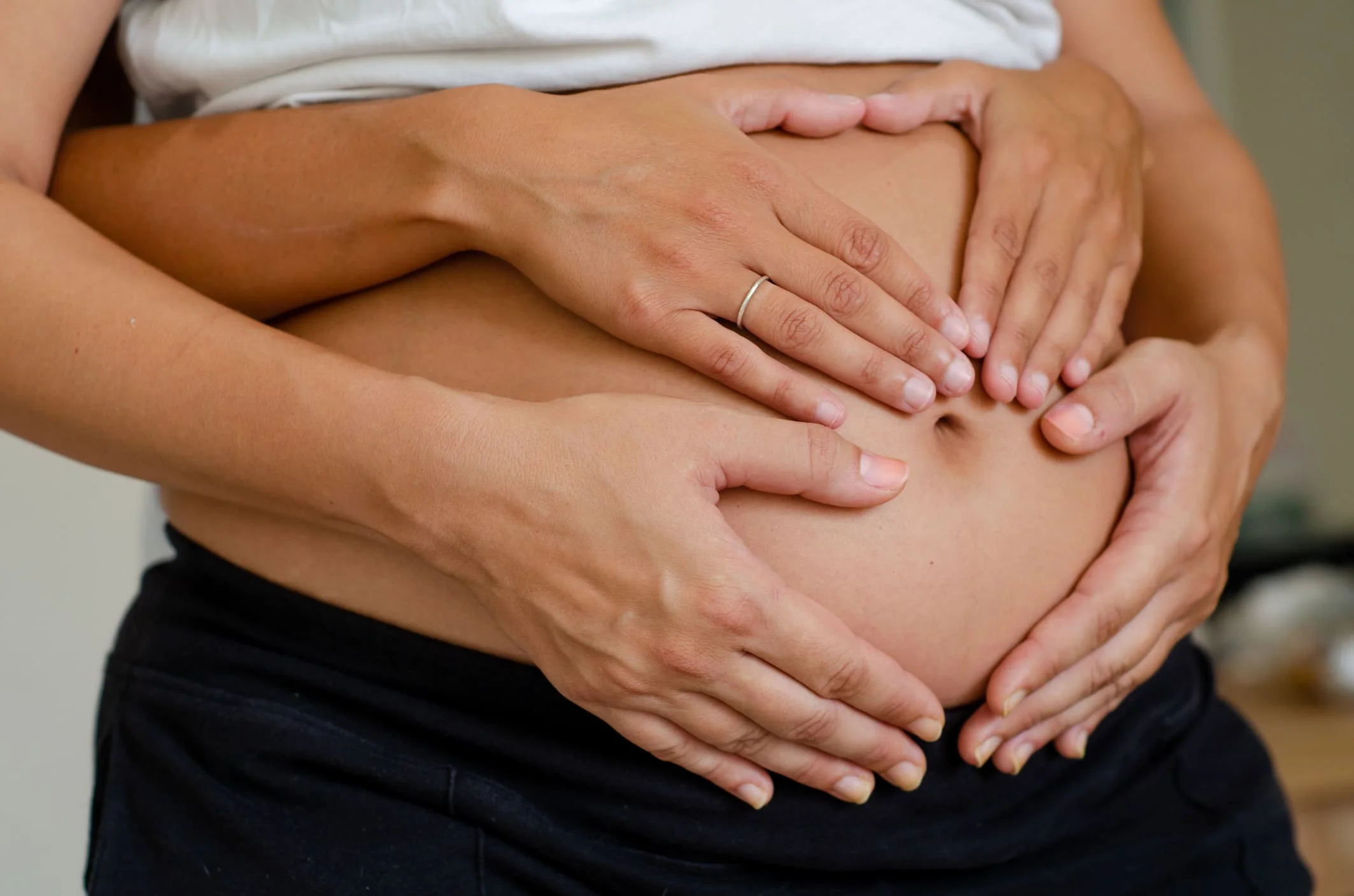 Detalle de un abdomen gestante en el segundo trimestre, con manos palpando la superficie para intentar sentir las primeras pataditas o movimientos fetales.
